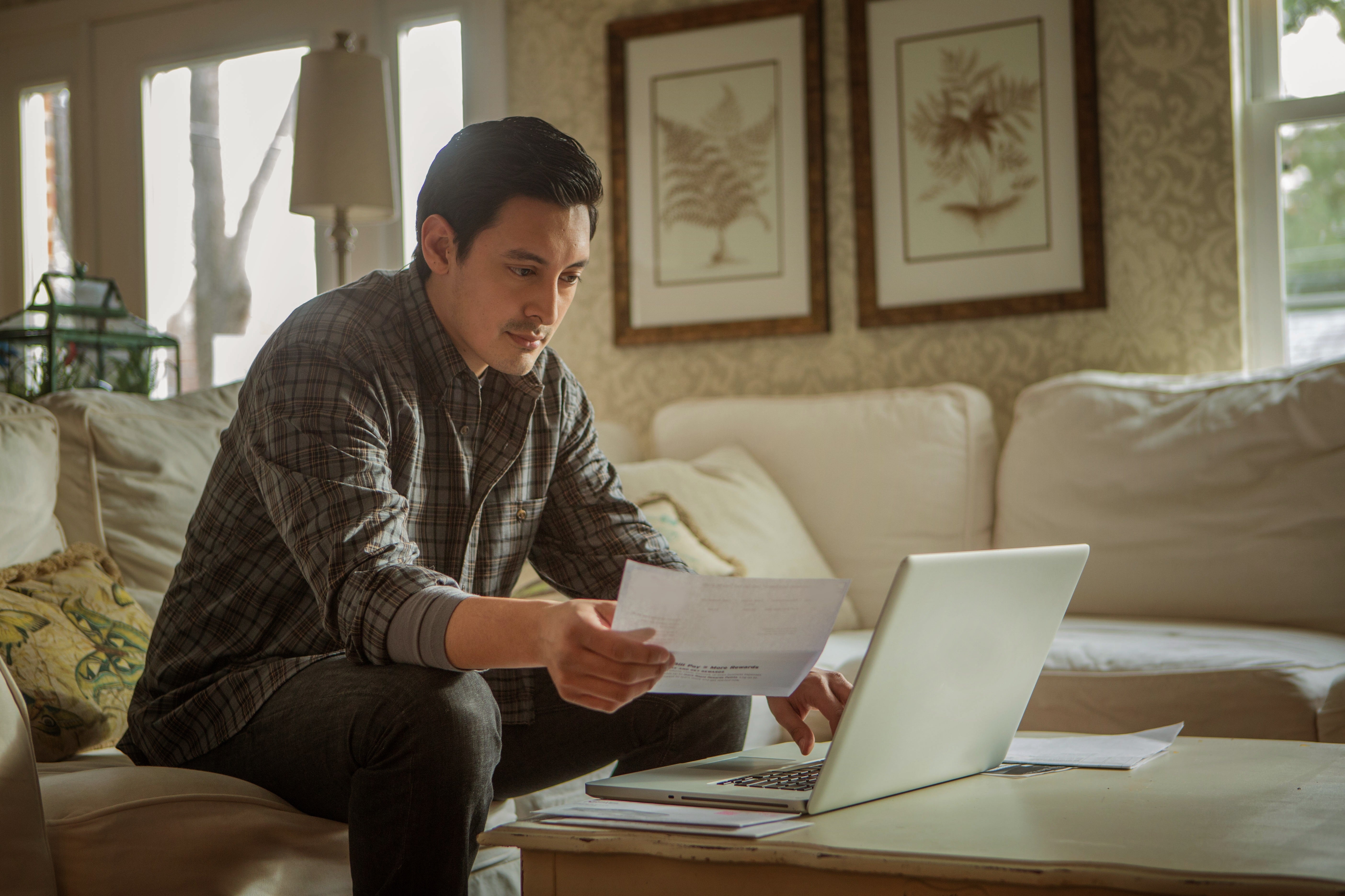 man looking at bills in front of a laptop